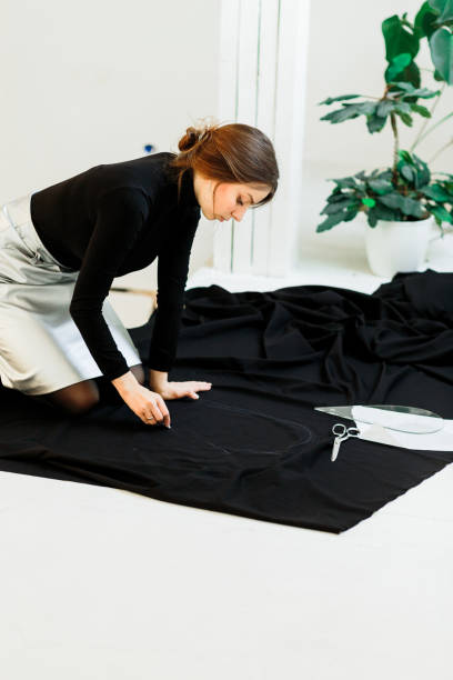 Beautiful seamstress, cut black fabric on the studio floor,draws on fabric